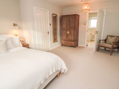 A bedroom with a bed armchair wooden wardrobe wall mirror and door leading to bathroom at Driftwood Sands Beadnell