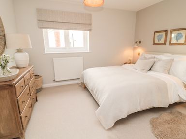 A bedroom with a bed a wooden dresser and a window at Driftwood Sands in Beadnell