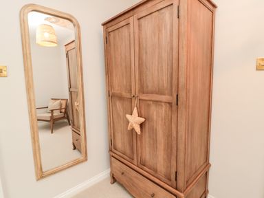 A wooden wardrobe with a star decoration and a tall mirror reflecting a chair with a cushion at Driftwood Sands in Beadnell