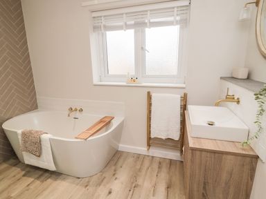 A bathroom with a bathtub a sink wooden vanity and a window at Driftwood Sands in Beadnell