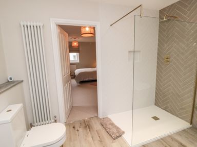 A bathroom with a toilet a radiator and a walk-in shower visible through an open door to a bedroom at Driftwood Sands in Beadnell