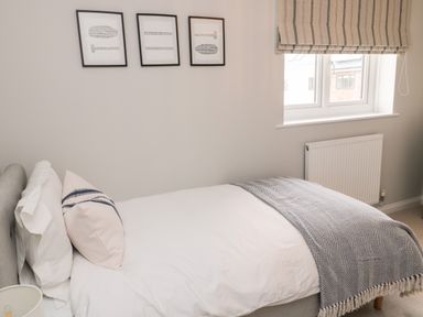 A bedroom with a single bed white bedding striped pillow and grey blanket three framed pictures above the bed and a window with striped blind at Driftwood Sands in Beadnell
