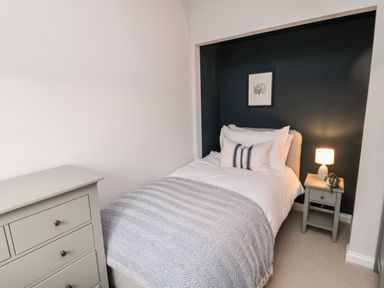 A bedroom with a single bed dresser and nightstand with lamp at Driftwood Sands in Beadnell