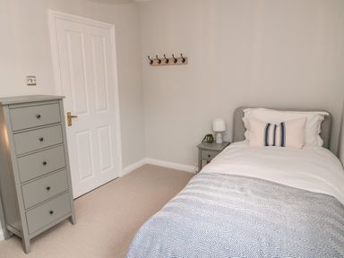 A bedroom with a single bed pillow bedside table lamp chest of drawers and a wall hook rack at Driftwood Sands in Beadnell