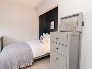A bedroom with a bed and a gray chest of drawers with an open mirror at Driftwood Sands in Beadnell