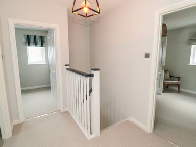 A hallway with two open doors showing rooms and a stair railing in Driftwood Sands Beadnell