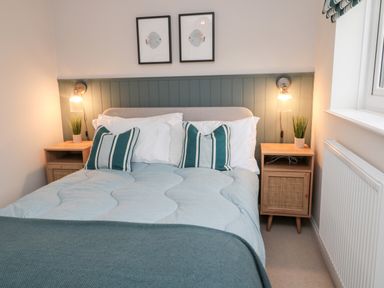 A bedroom with a bed a headboard two nightstands with plants and wall lights at Driftwood Sands Beadnell