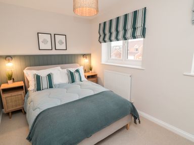 A bedroom with a bed and two bedside tables with lamps and plants at Driftwood Sands in Beadnell