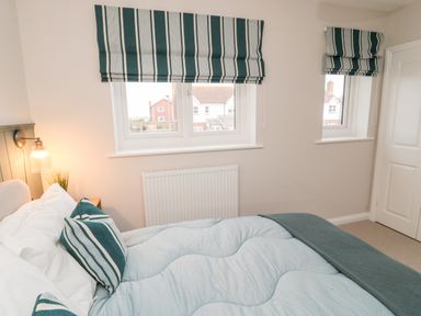 A bedroom with a bed next to two windows with striped blinds at Driftwood Sands in Beadnell