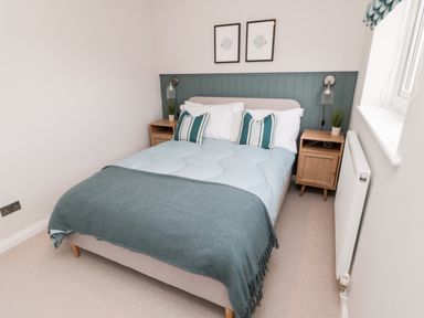 A bedroom with a bed with blue bedding and striped pillows two wooden bedside tables with plants and lamps at Driftwood Sands in Beadnell