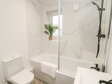 A bathroom with a toilet bathtub with towel potted plant and shower at Driftwood Sands in Beadnell