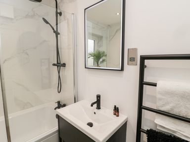 A bathroom with a bathtub shower combination a sink with black faucet and mirror and a towel rack with towels at Driftwood Sands Beadnell