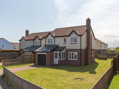A semi detached house with a garage and fenced garden in a residential area at Driftwood Sands in Beadnell