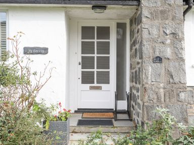 A white front door with glass panels and a letterbox between stone walls with plants outside at Ty Cerrig in Llanbedrog