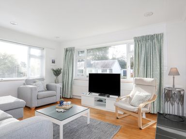 A living room with two armchairs a TV on a stand a coffee table and large windows with curtains at Ty Cerrig in Llanbedrog