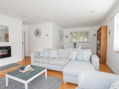 A living room with a gray sectional sofa a coffee table and a dining area in the background at Ty Cerrig in Llanbedrog