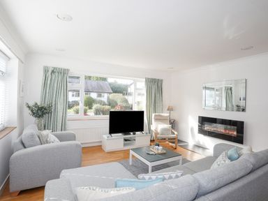 A living room with grey sofas a TV on a white stand and a wall-mounted electric fireplace at Ty Cerrig in Llanbedrog