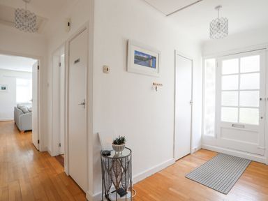 A hallway with wooden floor a small round table with a plant and a key hook beside a white front door at Ty Cerrig in Llanbedrog