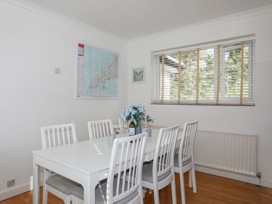 A dining room with a white table and six white chairs next to a window with blinds at Ty Cerrig in Llanbedrog