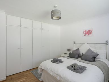 A bedroom with a double bed, white built-in wardrobes, bedside table with lamp, and a dragon picture on the wall at Ty Cerrig in Llanbedrog