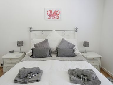 A bed with grey pillows and towels in a bedroom with white walls and bedside tables at Ty Cerrig in Llanbedrog