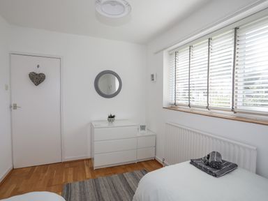 A bedroom with a bed a white dresser a round mirror and a window with blinds at Ty Cerrig in Llanbedrog