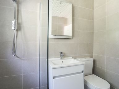 A bathroom with a shower, a sink with cabinet, a mirror, and a toilet at Ty Cerrig in Llanbedrog