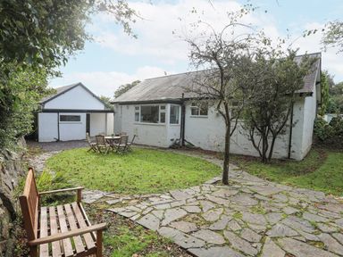 A house with a garden featuring a wooden bench a table with chairs a stone pathway and trees at Ty Cerrig in Llanbedrog
