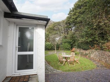 A garden with wooden chairs and a table on grass near a white building at Ty Cerrig in Llanbedrog