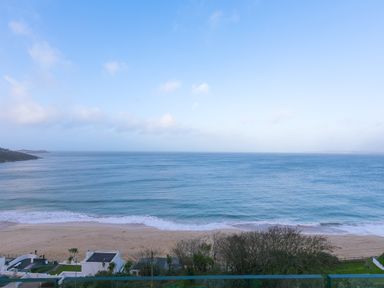 A beach with waves and a few buildings and trees near the shore at Wavetop in Carbis Bay