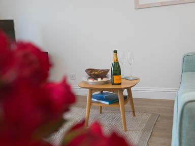 A small wooden table with a bottle of champagne two empty glasses a bowl of snacks and a plate of sushi in a living room at Wavetop in Carbis Bay