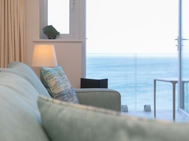 A living room with a sofa lamp and pillows by a window overlooking the sea at Wavetop in Carbis Bay