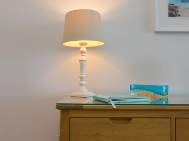 A wooden dresser with a white lamp a blue notebook and a blue glass decorative item on top at Wavetop in Carbis Bay