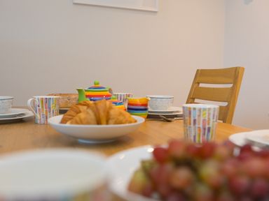 A wooden dining table set with croissants grapes colorful teapot and cups at Wavetop in Carbis Bay