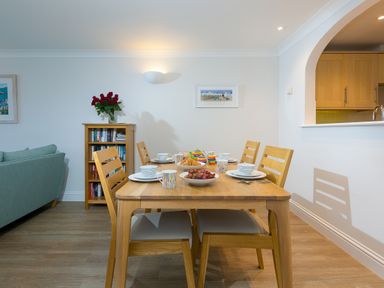 A dining area with a wooden table set with dishes and cups next to a bookshelf with flowers and a sofa at Wavetop in Carbis Bay