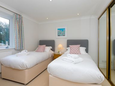 A bedroom with two single beds white bedding and towels bedside table with lamp and mirrored wardrobe at Wavetop in Carbis Bay