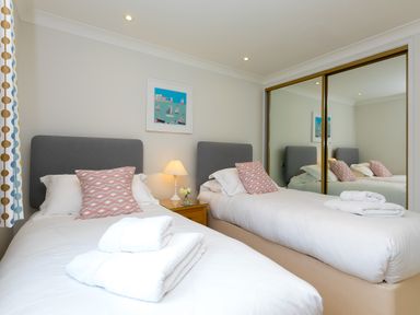A bedroom with two single beds a bedside table with a lamp and flowers and a large mirrored wardrobe at Wavetop in Carbis Bay