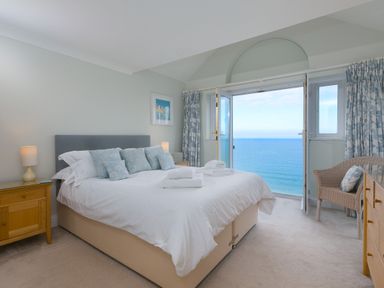 A bedroom with a bed facing open doors to the sea at Wavetop in Carbis Bay