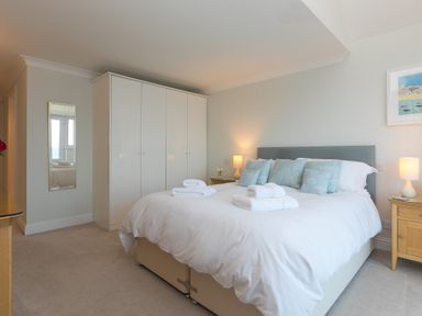 A bedroom with a large bed with white bedding and blue pillows next to wooden bedside tables with lamps and a white wardrobe at Wavetop in Carbis Bay