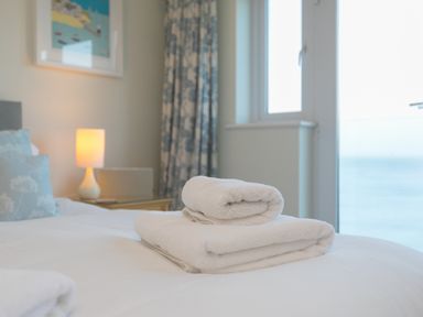 A bedroom with folded white towels on a bed next to a lamp and window at Wavetop Carbis Bay