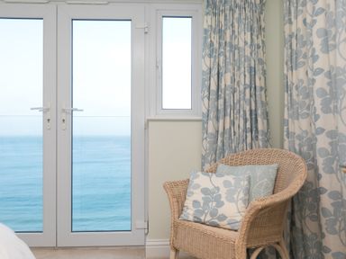A wicker chair with cushions next to glass doors showing an ocean view at Wavetop in Carbis Bay