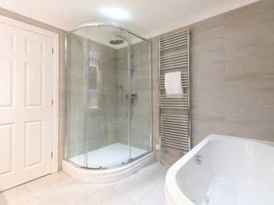 A bathroom with a glass enclosed shower a white bathtub a towel rack with a towel and a closed door at Wavetop in Carbis Bay
