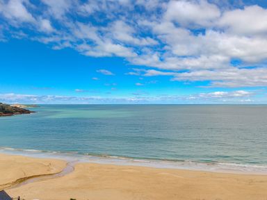 A sandy beach with a small stream flowing into the sea and a partly cloudy sky at Wavetop in Carbis Bay