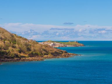 A coastal landscape with houses on cliffs and a lighthouse by the sea at Wavetop in Carbis Bay