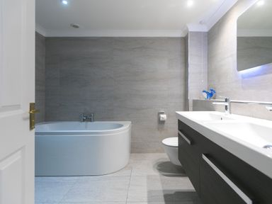 A bathroom with a white bathtub a wall-mounted toilet a double sink vanity and a mirror at Wavetop in Carbis Bay