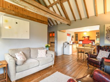 A living room with a beige sofa and wooden table connected to a kitchen with wooden cabinets and dining table at The Old Dairy Whitchurch Canonicorum near Charmouth