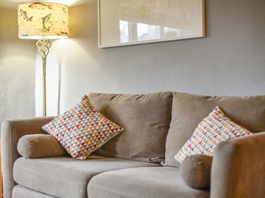 A beige sofa with patterned cushions and a floor lamp with fish designs in a living room at The Old Dairy Whitchurch Canonicorum near Charmouth