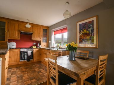 A kitchen with wooden cabinets and table with yellow flowers on it at The Old Dairy in Whitchurch Canonicorum near Charmouth