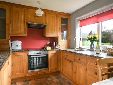 A kitchen with wooden cabinets granite countertops a built in oven a sink and a window with red blinds at The Old Dairy in Whitchurch Canonicorum near Charmouth