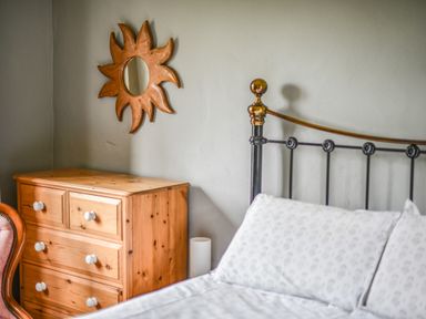 A bedroom with a wooden chest of drawers a sun-shaped wall mirror and a metal bed frame at The Old Dairy in Whitchurch Canonicorum near Charmouth